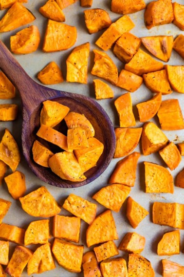 Wood spoon scooping up chunks of roasted sweet potatoes on a sheet pan.