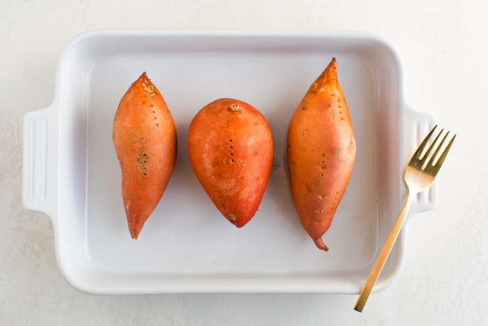 Three sweet potatoes pierced with a fork in a baking dish.