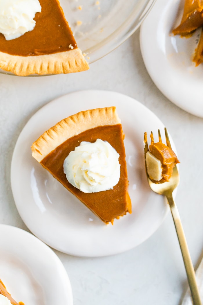 Slice of sweet potato pie topped with whipped cream. A bite is taken out of the pie.