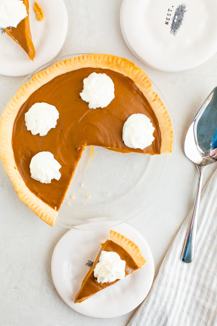 Sweet potato pie topped with whipped cream. A slice is taken out of the pie and is on a plate.