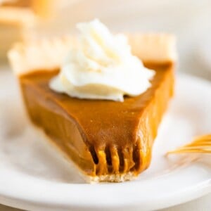 Slice of sweet potato pie topped with whipped cream. A bite is taken out of the pie.