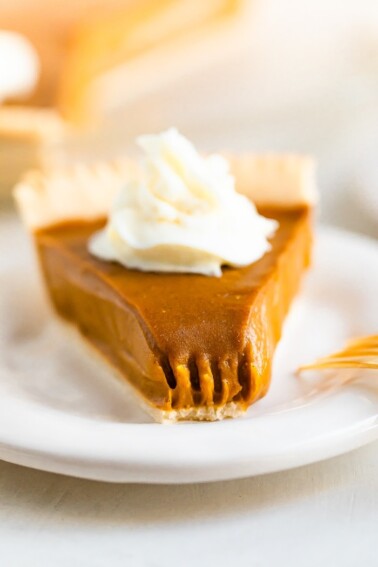 Slice of sweet potato pie topped with whipped cream. A bite is taken out of the pie.