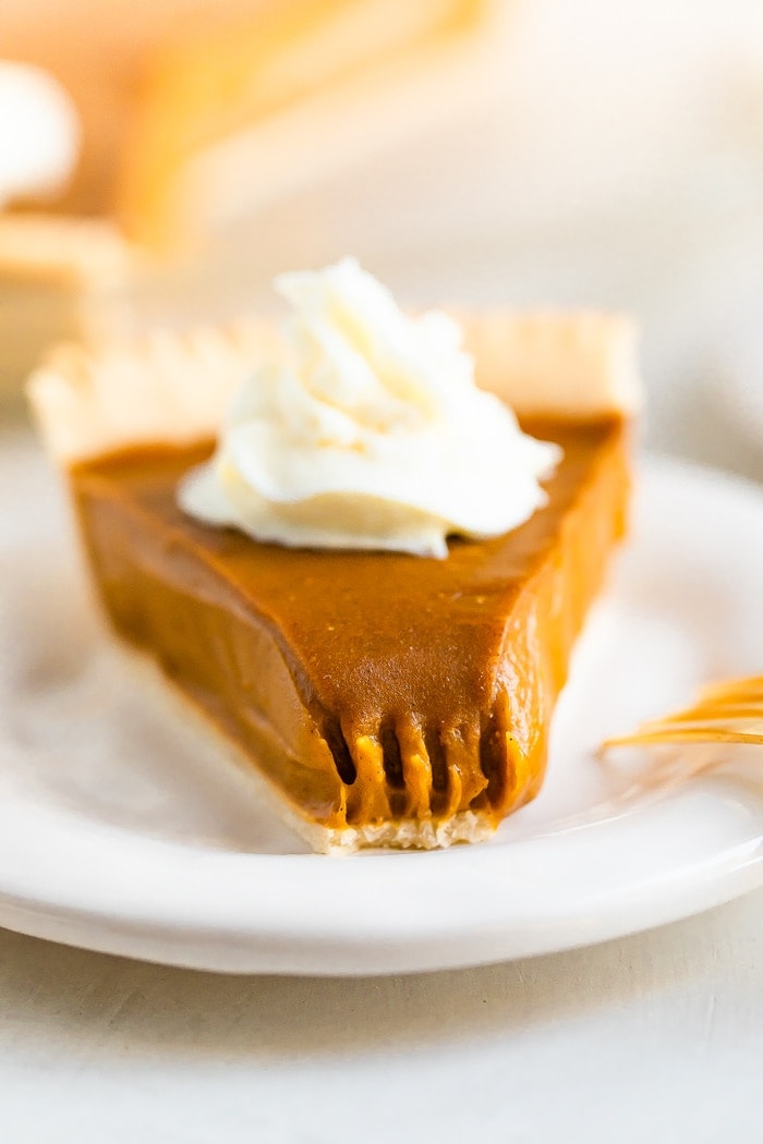 Slice of sweet potato pie topped with whipped cream. A bite is taken out of the pie.