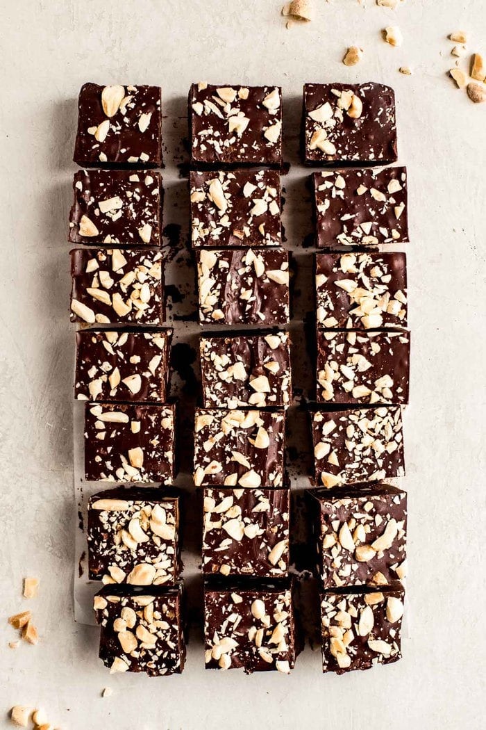 Squares of chocolate fudge topped with chopped peanuts on a countertop.