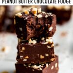 Stack of three squares of fudge studded with chopped peanuts. The top piece of fudge has a bite taken out of it.