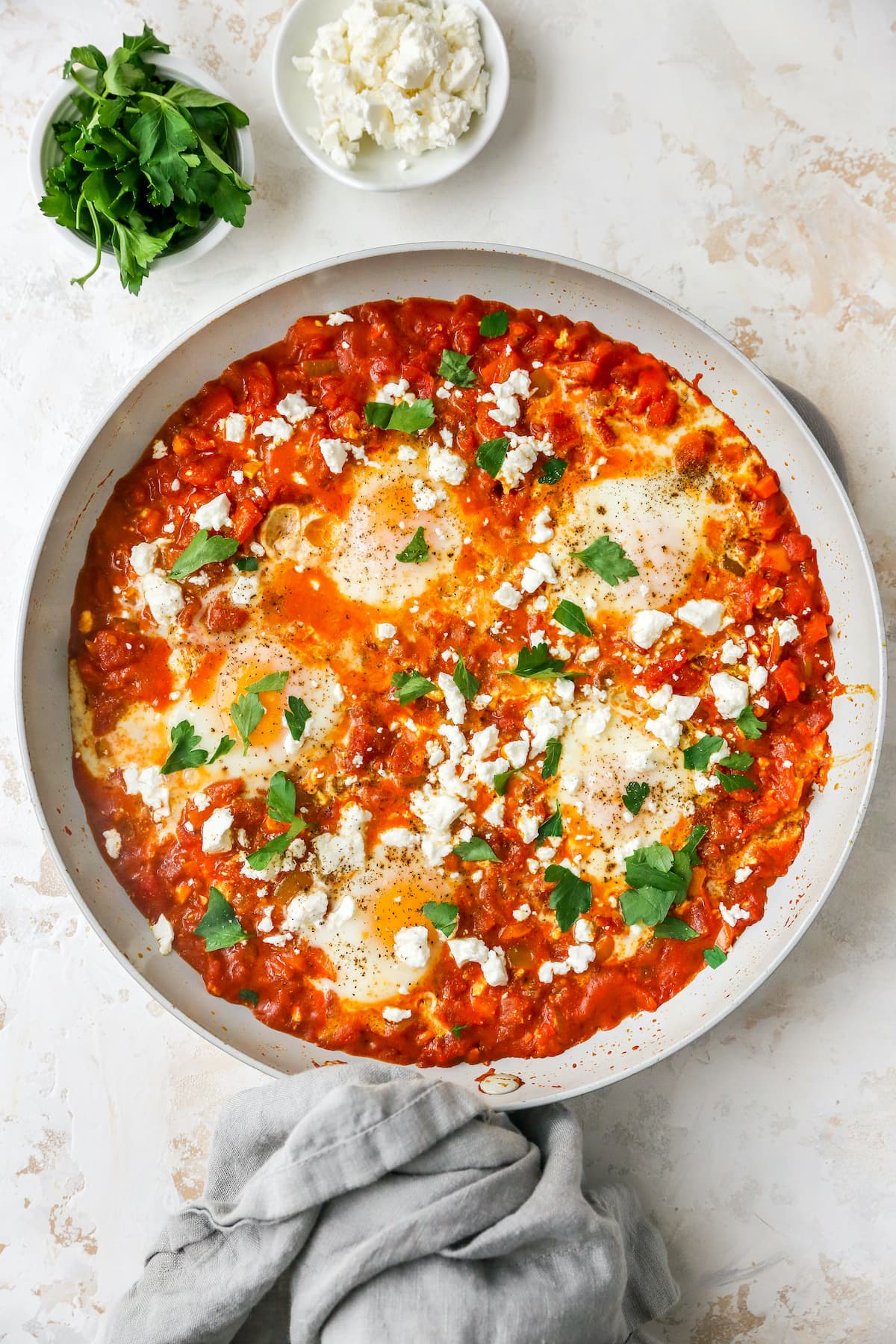 Cooked shakshuka in a sauté pan with fresh herbs and feta on top.