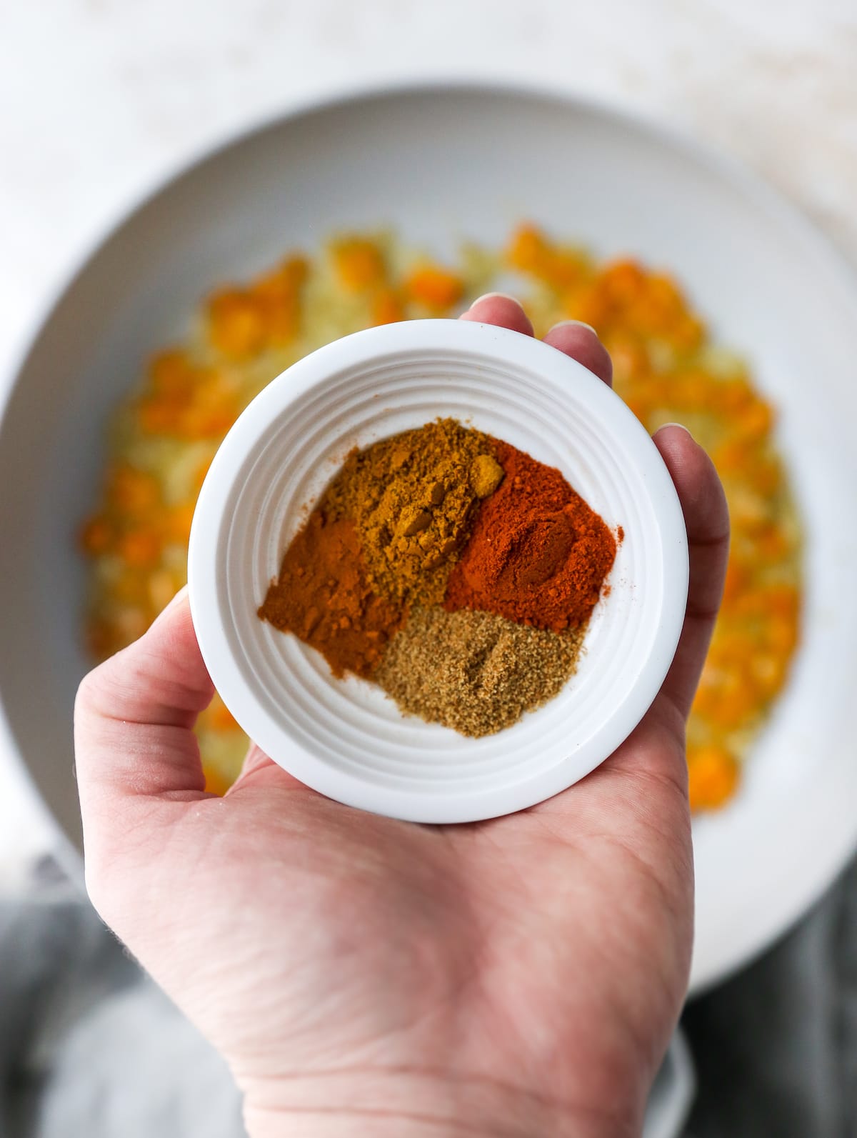 Four spices for shakshuka in s small white bowl in a woman's hand.