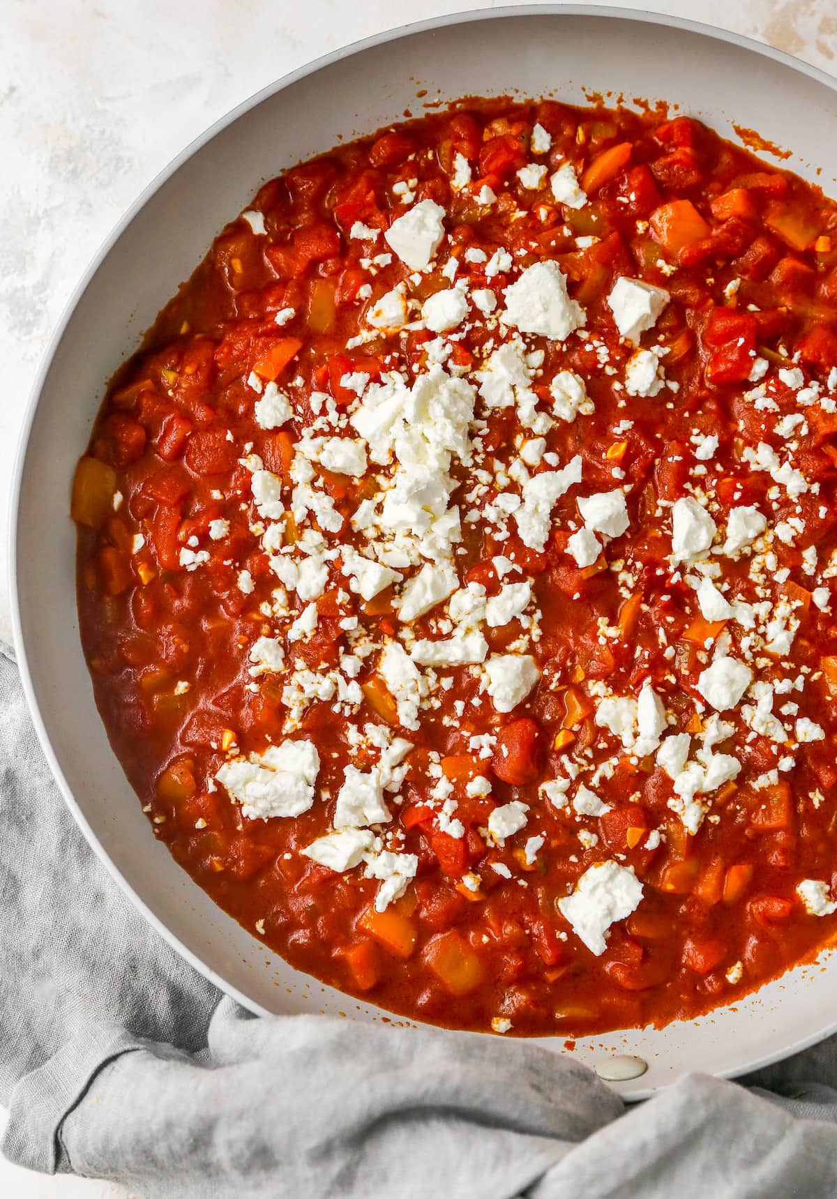 Tomato sauce for shakshuka in a sauté pan with feta sprinkled on top.