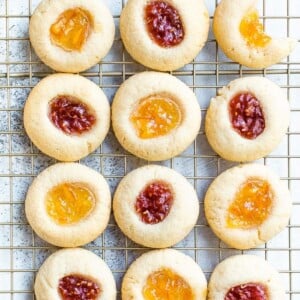 Almond flour thumbprint cookies on a cooling rack. Some have raspberry jam and some have orange marmalade.