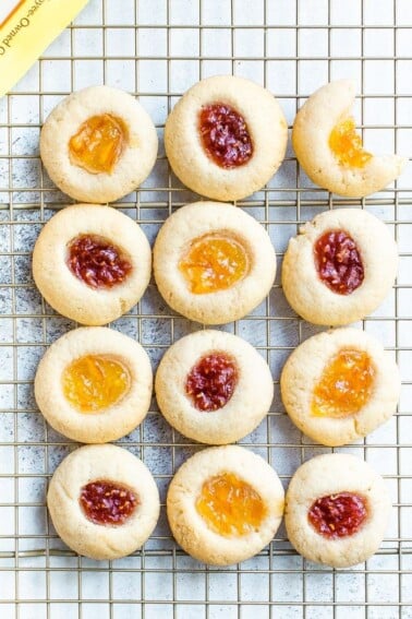 Almond flour thumbprint cookies on a cooling rack. Some have raspberry jam and some have orange marmalade.