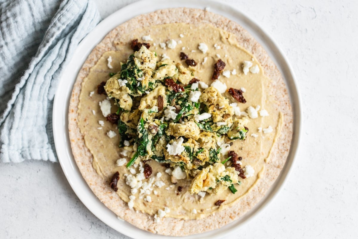 Wrap topped with hummus, eggs, cheese, spinach and sun-dried tomatoes.