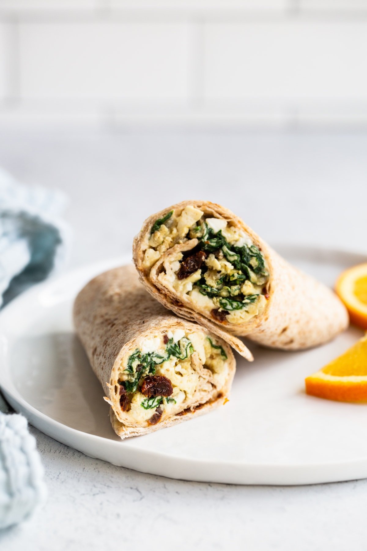 Egg breakfast wrap on a plate with orange slices.