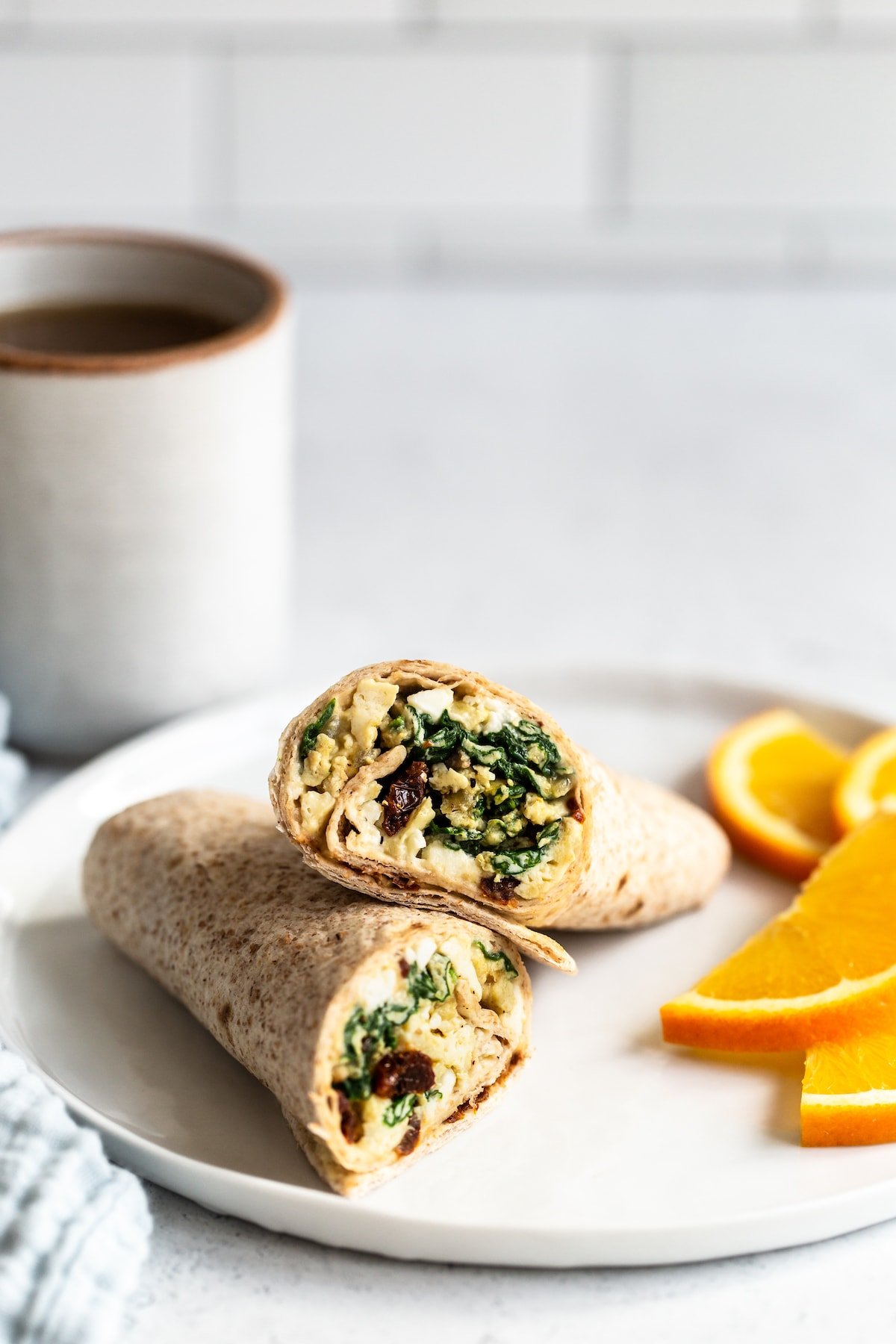 Egg breakfast wrap on a plate with orange slices.
