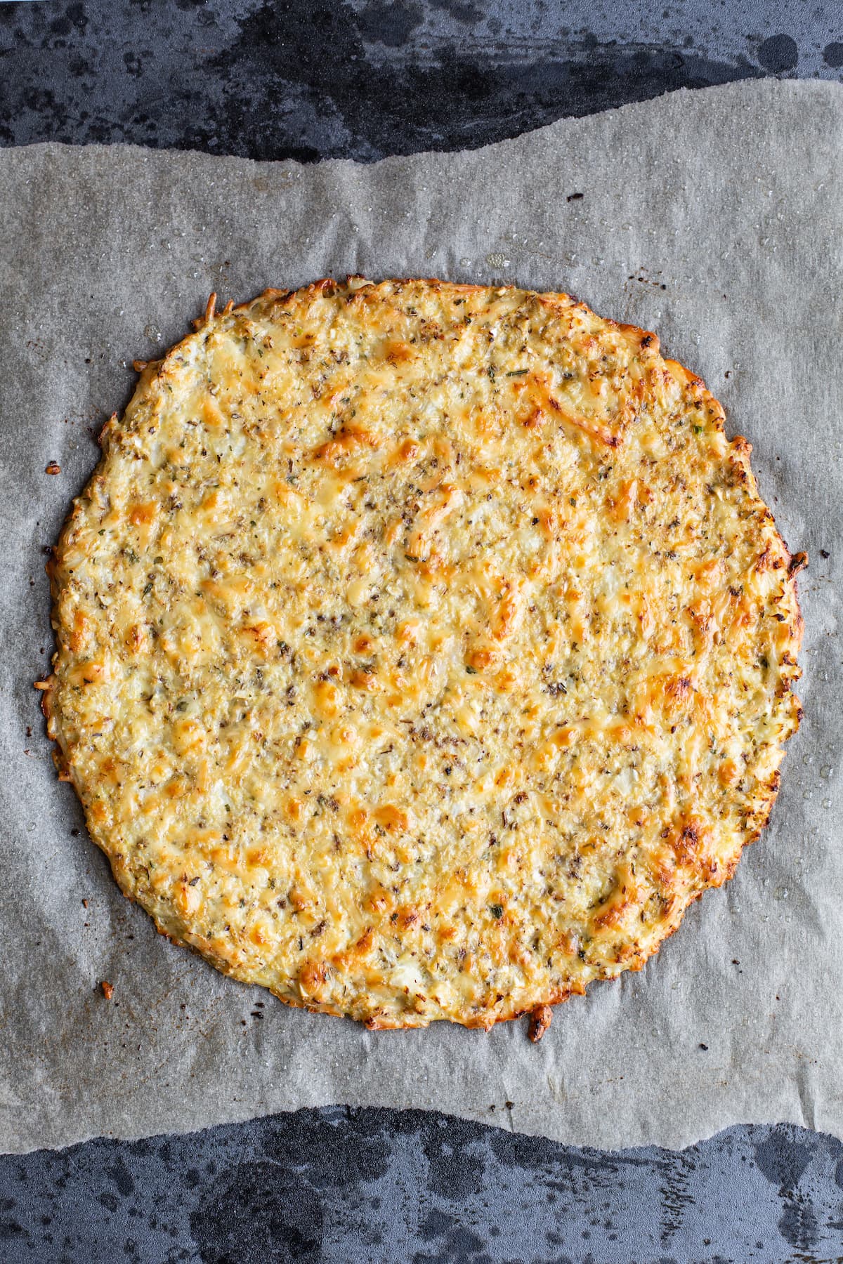 Baked cauliflower pizza crust on parchment paper.