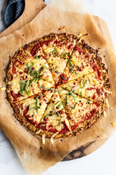 Cauliflower pizza on parchment paper and a wood pizza paddle.