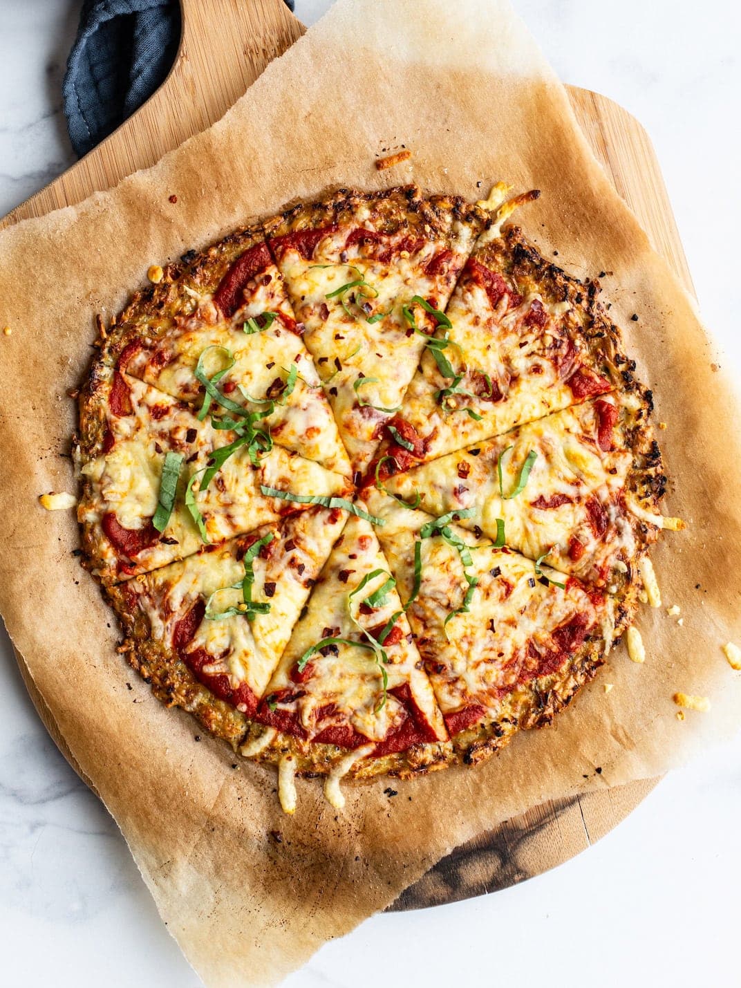 Cauliflower pizza on parchment paper and a wood pizza paddle.