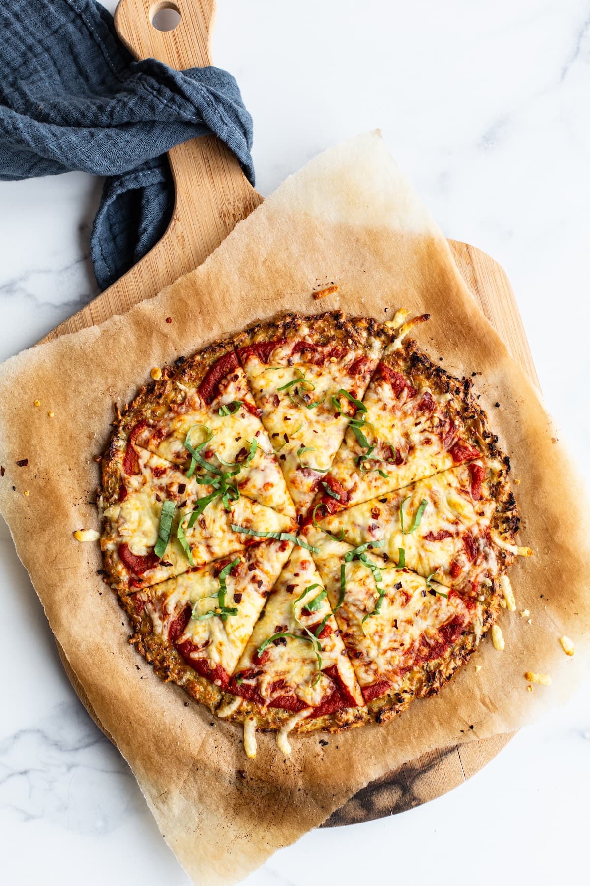 Cauliflower pizza on parchment paper and a wood pizza paddle.