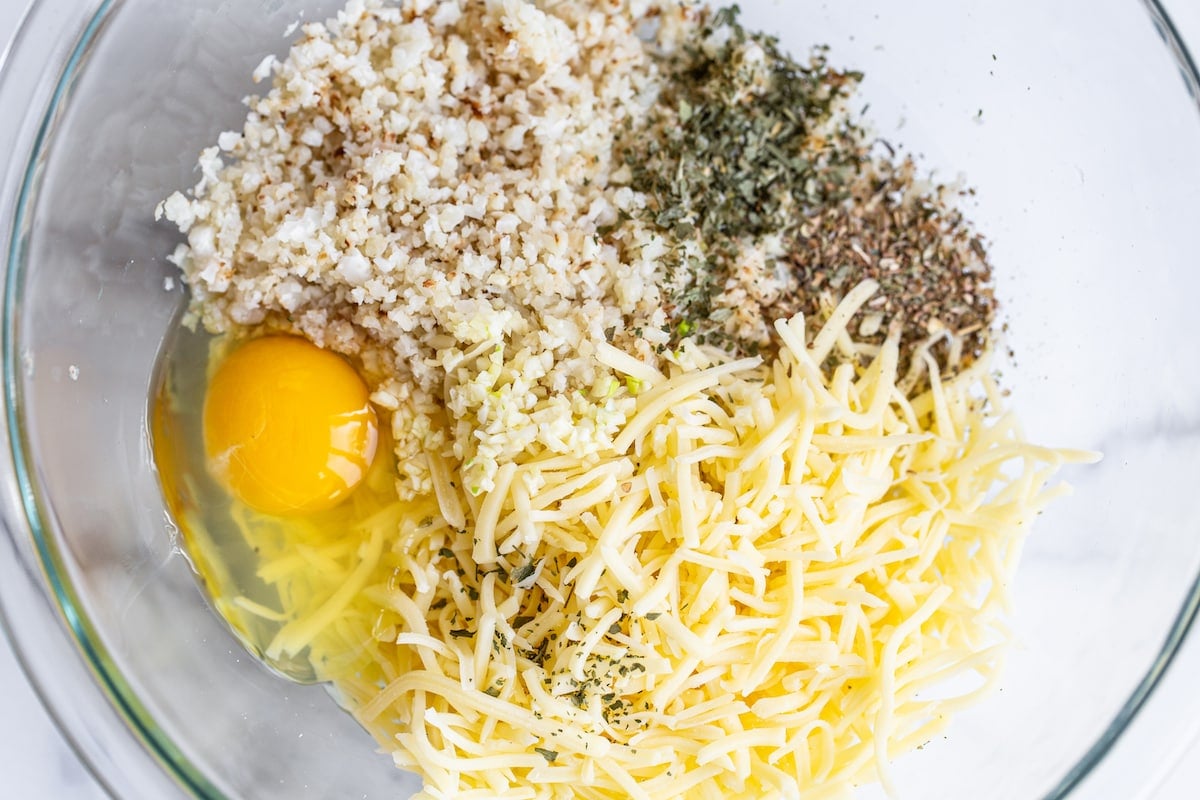 Cauliflower, spices, and egg and cheese in a mixing bowl.