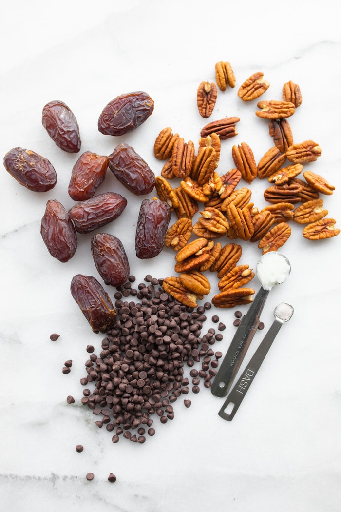 Dates, pecans, chocolate chips, coconut oil and sea salt on a marble table top.