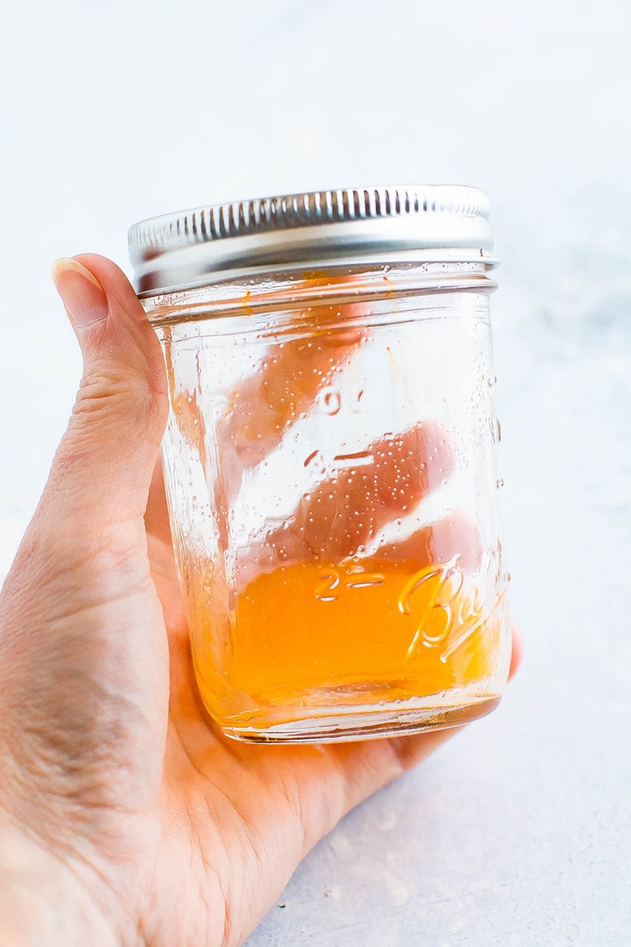Hand holding a mason jar with a orange electrolyte powder dissolved in a little water.