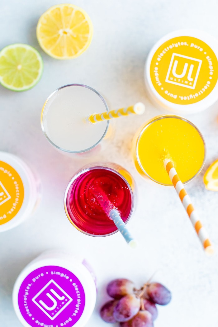 Three glasses of electrolyte soda and containers of electrolyte powder.