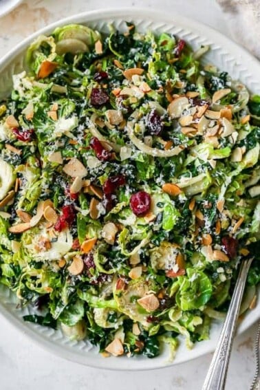 Kale and brussels sprout salad in a bowl with serving spoons.