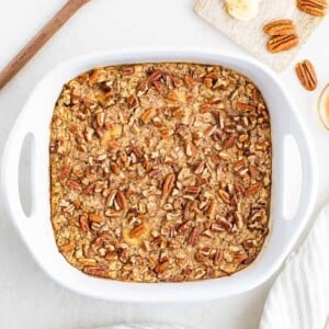 Maple pecan baked oatmeal in a white baking dish with bananas and pecans.