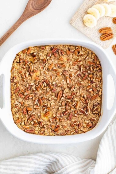 Maple pecan baked oatmeal in a white baking dish with bananas and pecans.