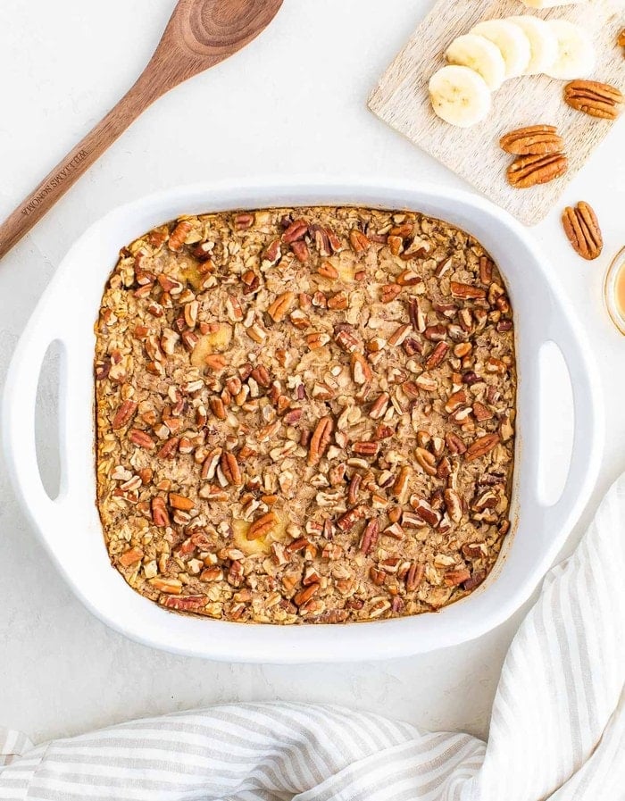 Maple pecan baked oatmeal in a white baking dish with bananas and pecans.