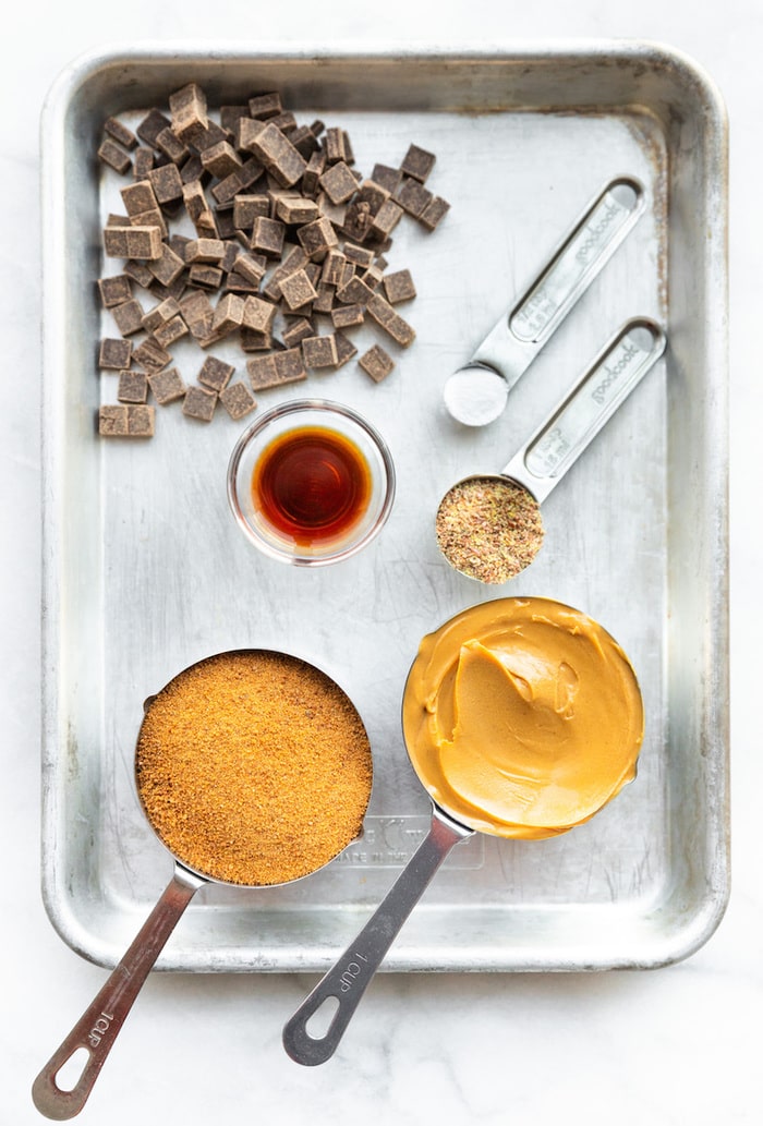 Cookie tray with ingredients to make peanut butter blossom cookies: chocolate chunks, salt, flax, vanilla, coconut sugar and peanut butter.