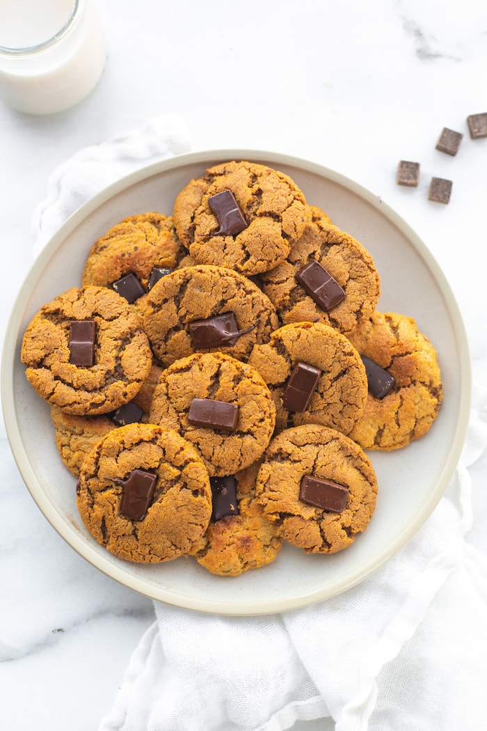 Plate full of peanut butter blossoms. A glass of milk and a few chocolate chunks are beside the plate.