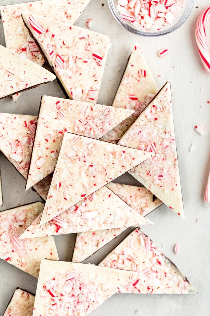 Triangles of peppermint bark on a table surrounded but crushed candy cane.