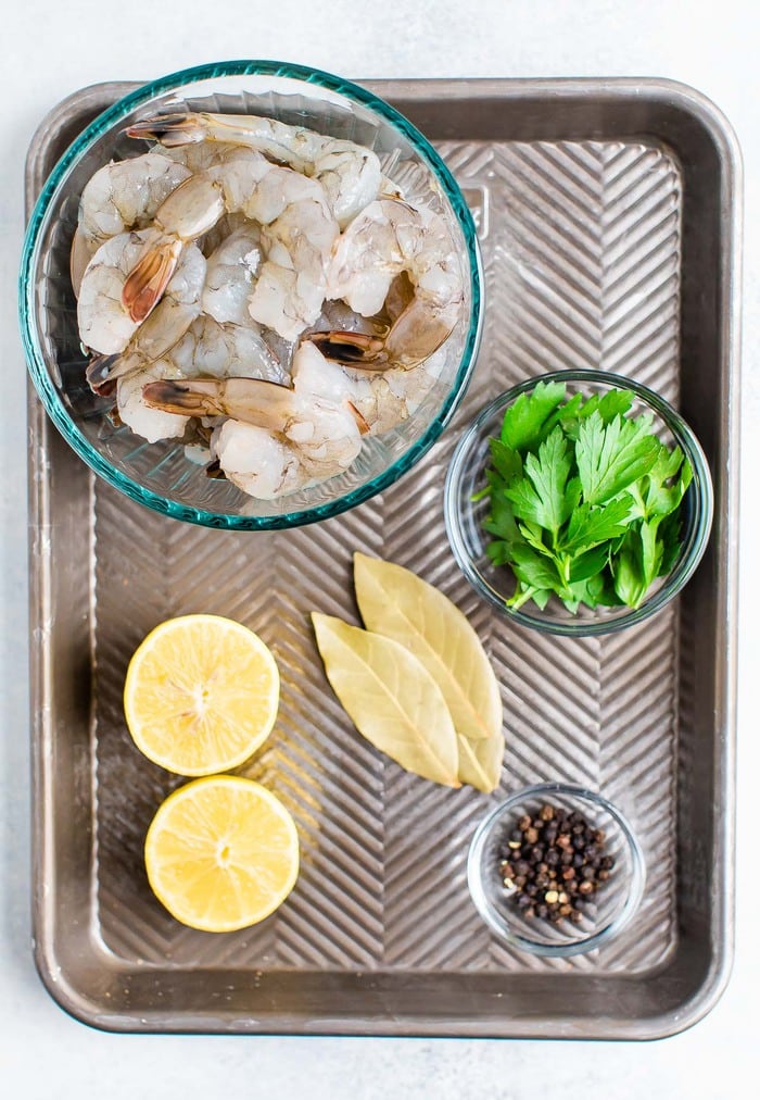 Shrimp, parsley, bay leaves and peppercorn measured and on a metal sheet.