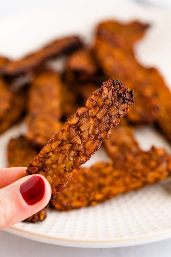 Hand holding a slice of homemade tempeh bacon.