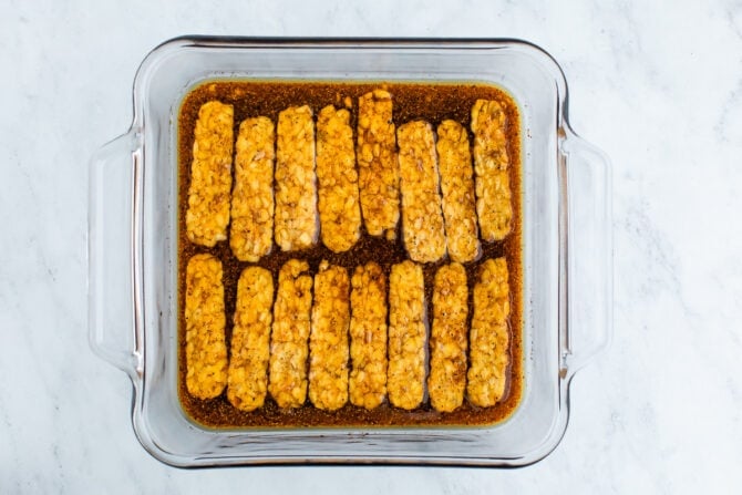 Slices of tempeh marinating in a glass pan.