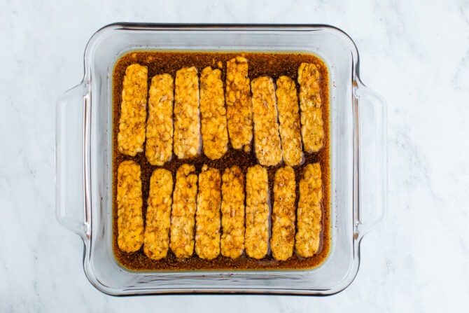 Slices of tempeh marinating in a glass pan.