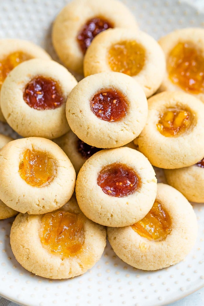 Almond flour thumbprint cookies on a polka dot plate. Some have raspberry jam and some have orange marmalade.