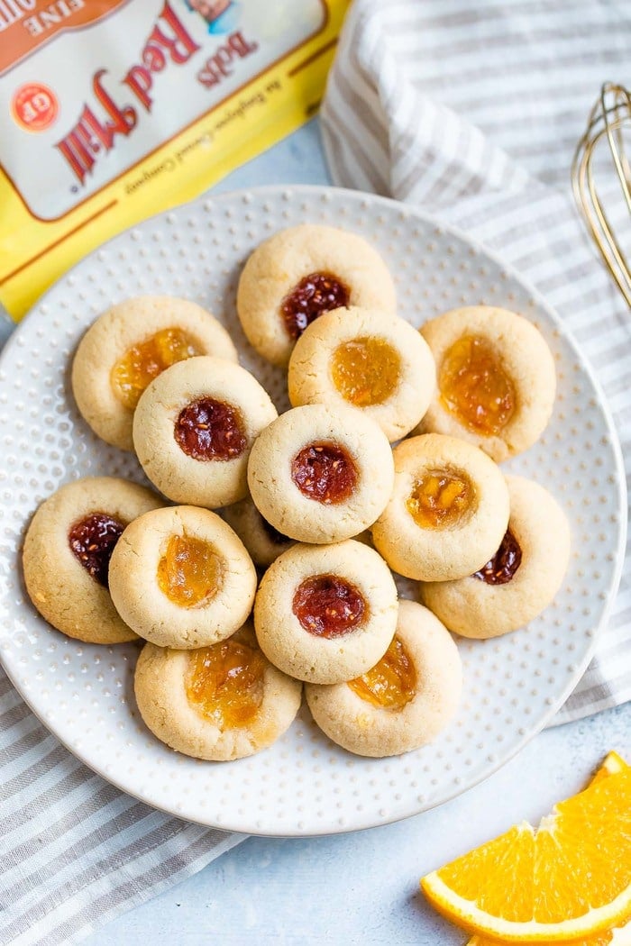 Almond flour thumbprint cookies on a polka dot plate. Some have raspberry jam and some have orange marmalade.