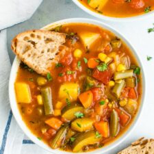 Bowl of vegetable soup served with slices of bread.
