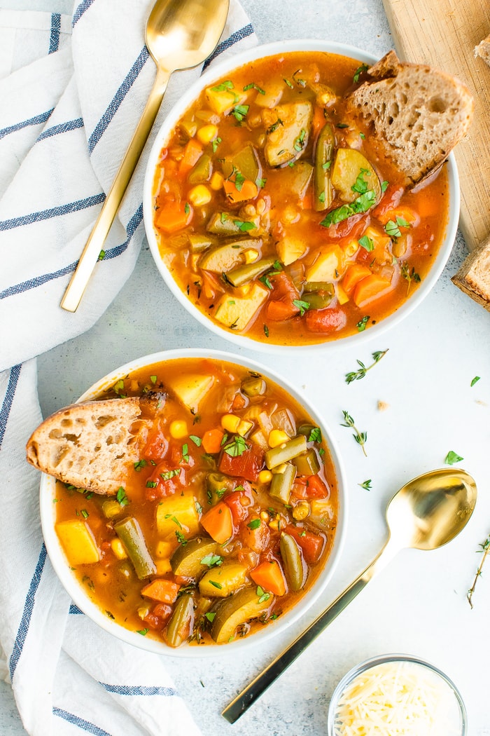 Two bowls of vegetable soup served with crusty bread.