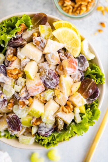 Waldorf salad served in a bowl over lettuce garnished with lemon.