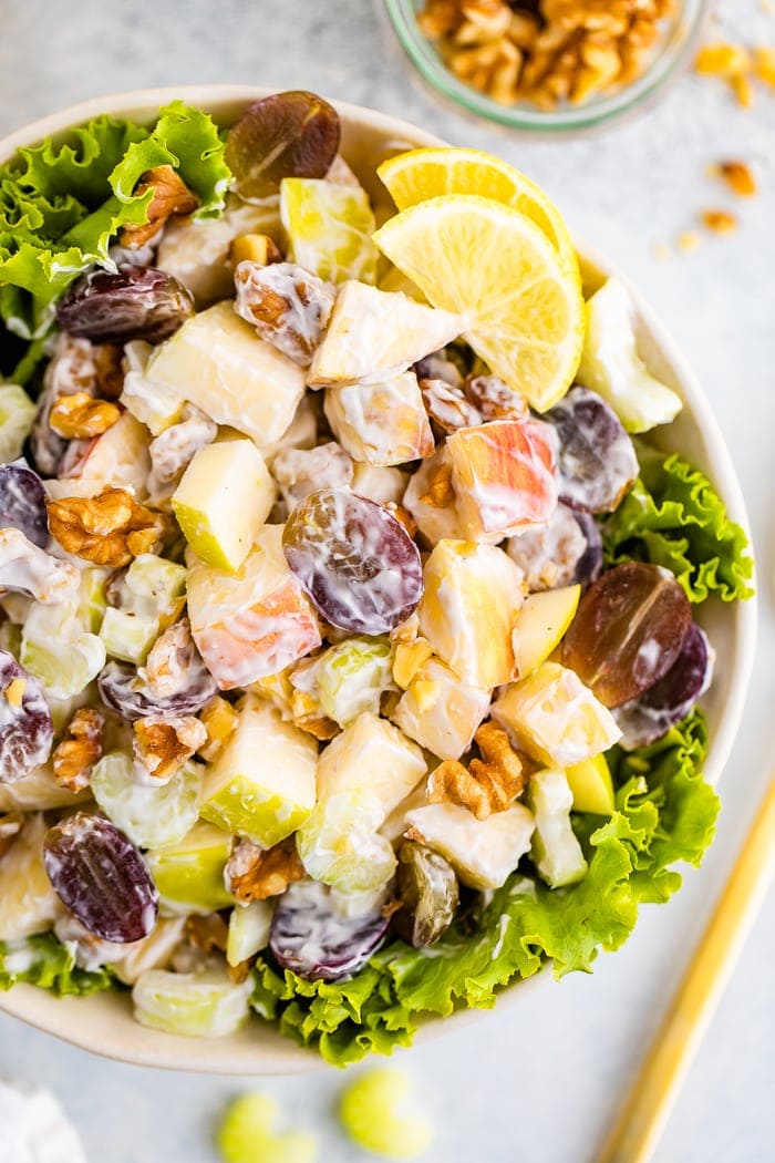 Waldorf salad served in a bowl over lettuce garnished with lemon.