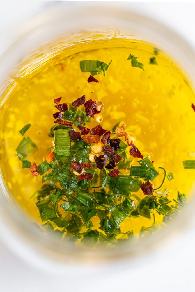 Olive oil, vinegar, garlic, red pepper flakes and green onion in a glass jar.