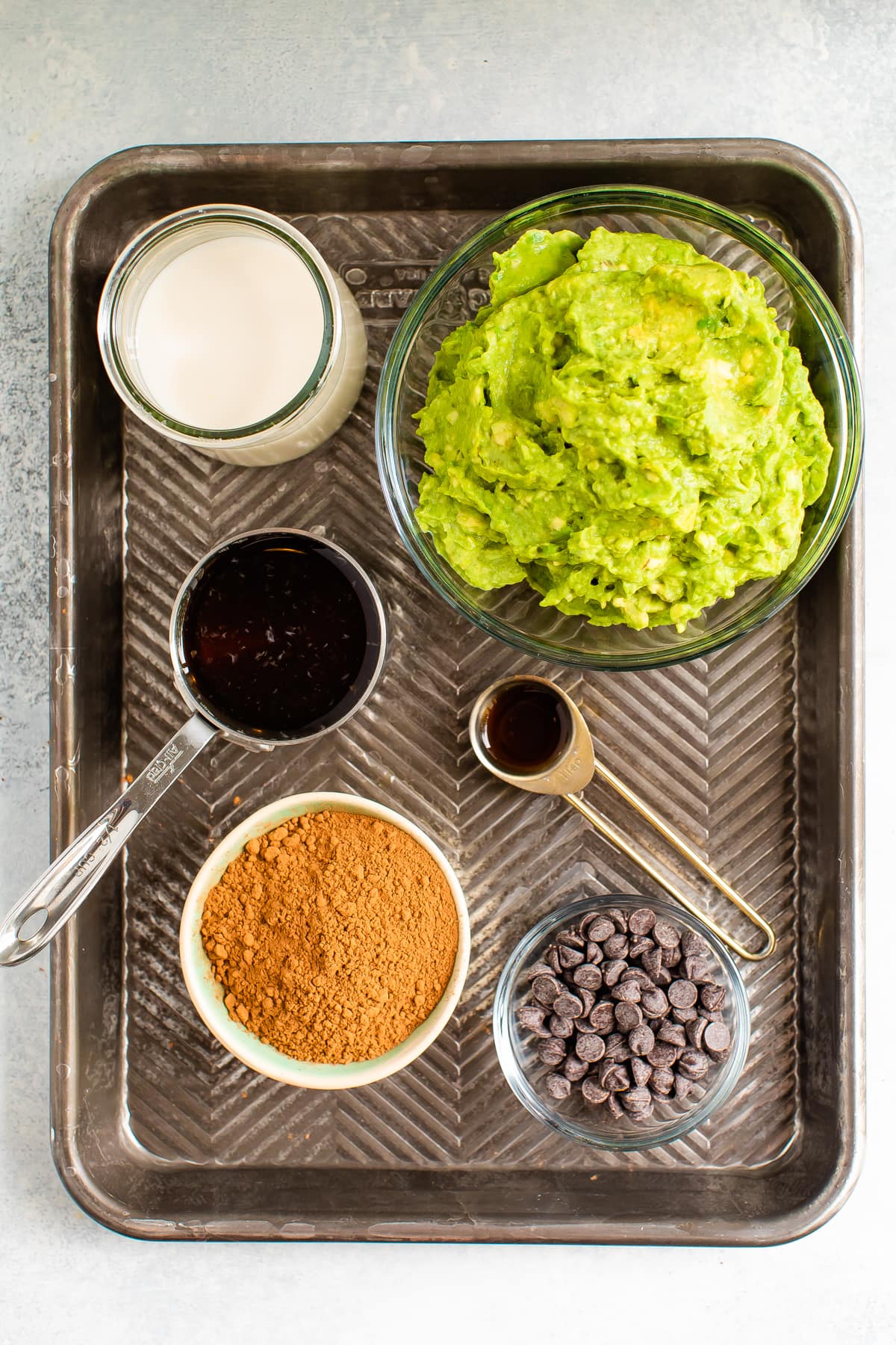 Ingredients for avocado pudding on a tray - almond milk, maple syrup, cocoa powder, avocado, vanilla and chocolate chips