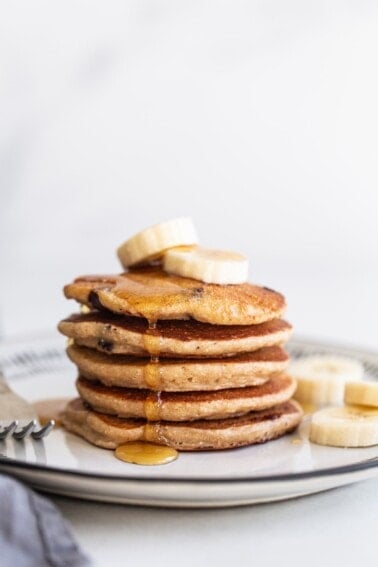 Stack of banana chocolate chip pancakes topped with banana slices and maple syrup.