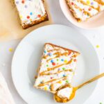 Slice of birthday cake baked oatmeal topped with frosting, nut butter drizzle and sprinkles. A spoon has taken a bite out of it.