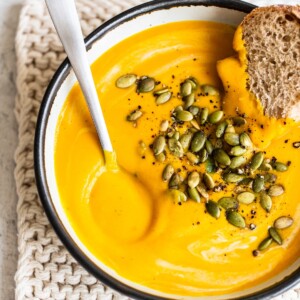 Soup bowl with butternut squash soup, a spoon and some bread.