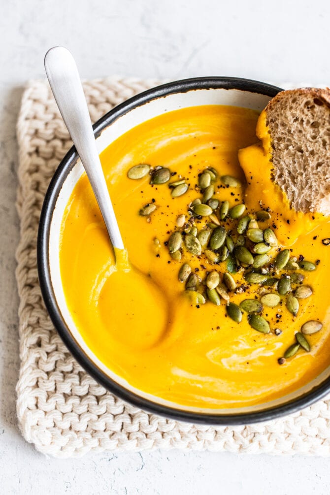 Soup bowl with butternut squash soup, a spoon and some bread.