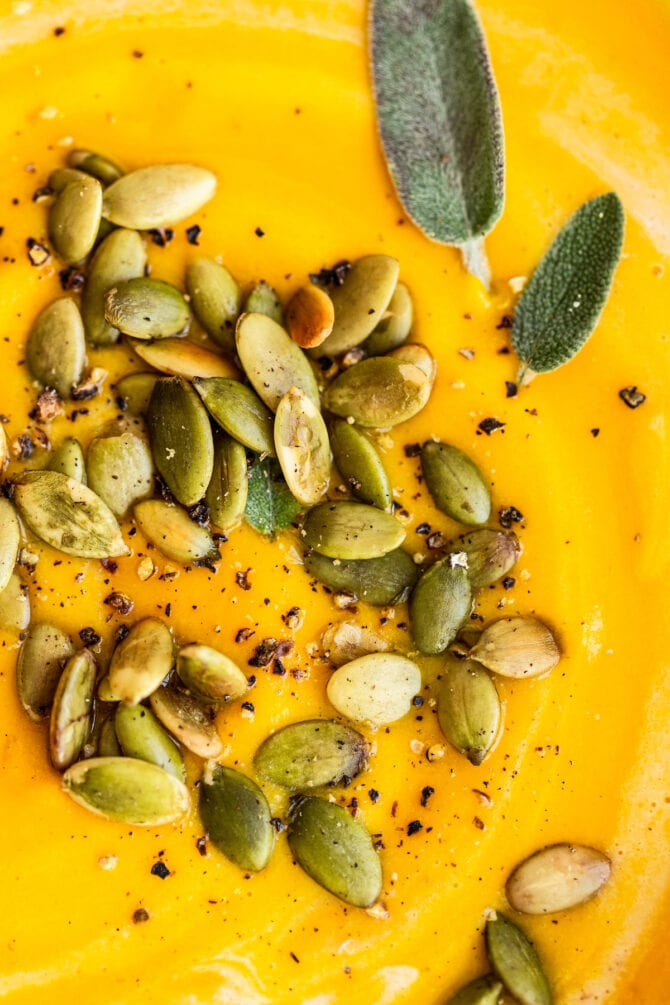 Close up photo of butternut squash soup topped with pepitas, pepper and sage.