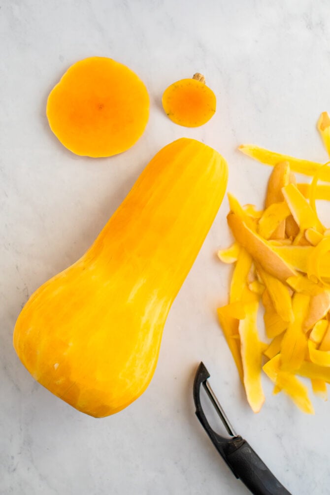 Vegetable peeler and peels next to a peeled butternut squash.